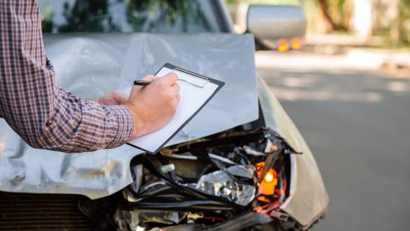 Photo of a man filling papers next to damaged car